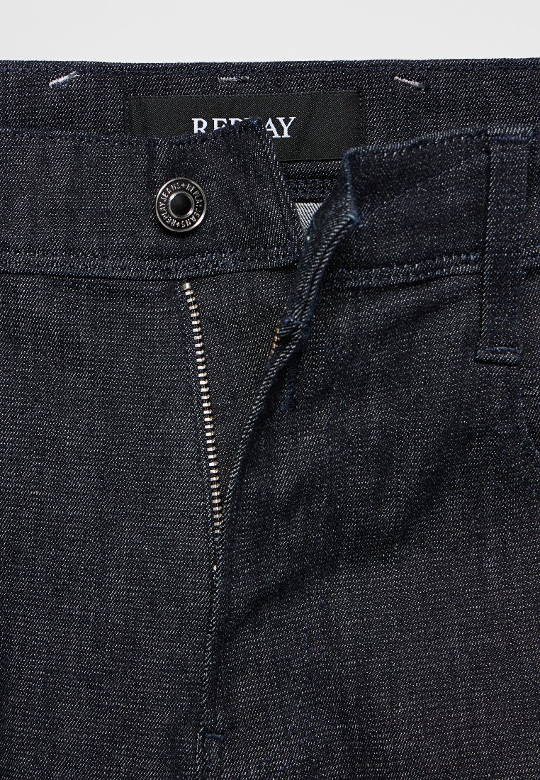 Dunkelblaue Jeans aus Denim mit Reißverschluss, ausgestattet mit einem runden Metallknopf und einem im Taillenbund genähten Markenlabel.