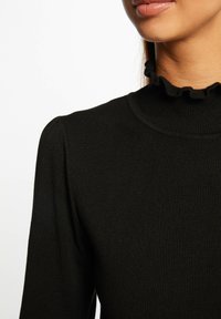 Top negro de cuello alto con textura acanalada y un cuello con volantes, con mangas ajustadas y una superficie lisa. Sin patrones visibles ni adornos.