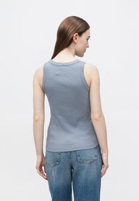 Szary prążkowany top na ramiączkach z okrągłym dekoltem, bez rękawów, o dopasowanym kroju. Noszony z wysokim stanem niebieskich dżinsów.