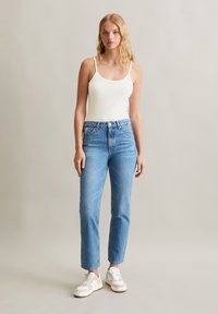 Witte geribbelde tanktop, hoog-waisted lichtblauwe spijkerbroek en witte sneakers. Rechte pijpen met een lichte slijtage aan de zoom.