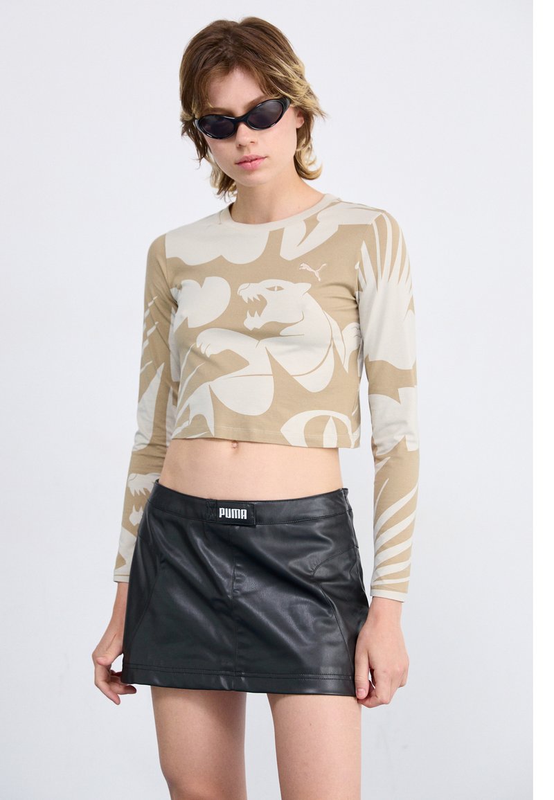 Beige long-sleeve crop top with abstract tan patterns, paired with a black faux leather mini skirt featuring a visible logo on the waistband.