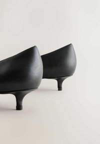 Svarta högklackade läderskor med slät textur, spetsig tåkonstruktion och smala klackar. Två par vinklade för djup.