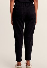 Schwarze tapered Hosen mit elastischem Taillenbund, umgeschlagenen Säumen und zwei Gesäßtaschen, aus glattem, strapazierfähigem Stoff gefertigt.