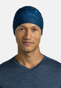 Blue fabric beanie with a smooth texture and a marbled design, worn by a person in a gray V-neck shirt, facing forward.