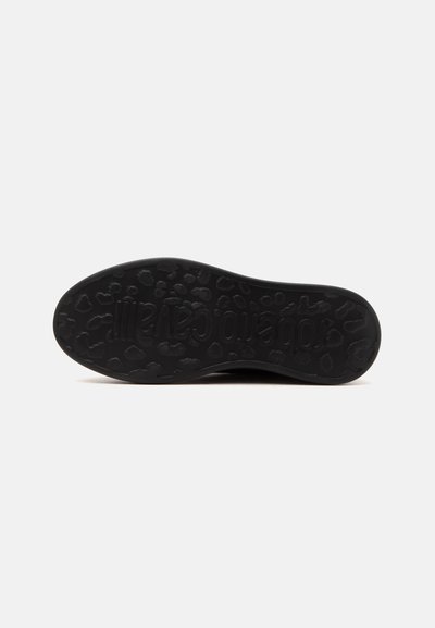 Semelle de chaussure noire avec un motif léopard et un texte embossé inversé visible en dessous.