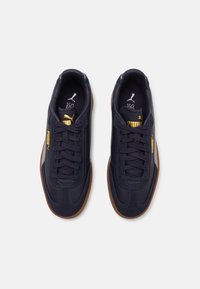 Pair of dark blue Puma sneakers with gum soles, gold Puma logos on tongues and sides, and black laces, viewed from above on white background.