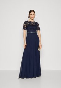 Navy-iltaasu, jossa on pitsihihat ja koristeltu vyötärö. Valoisa sifonkihame, muotoiltu yläosa ja pyöreä pääntie. Mukana on clutch.