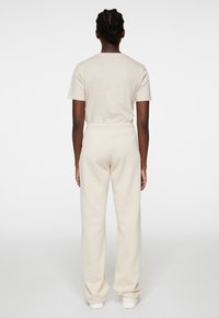 Helles beige T-Shirt in lockerer Passform und Hose mit elastischem Bund, die eine glatte Textur und ein einfaches Design aufweisen, kombiniert mit weißen Schuhen.