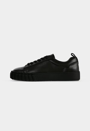 Black low-top leather sneaker with thick sole, side laces, pull tab at heel, and subtle branding on side panel.