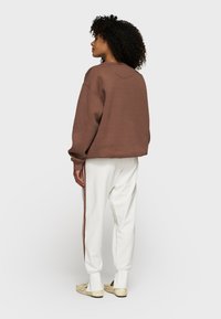 Brauner übergroßer Sweatshirt mit lockerer Passform, kombiniert mit weißen Jogginghosen mit braunem Seitenstreifen und bündchenabgeschlossenen Säumen.