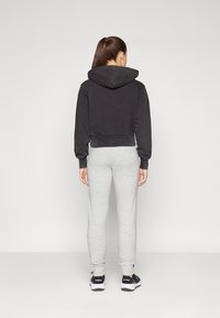 Kuttet svart hettegenser med hette og elastisk kant, kombinert med lys grå joggebukser med en tettsittende design og ribbede ankelmansjetter.
