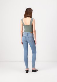 Vaaleanvihreä hihaton bodysuit pitsisillä olkaimilla yhdistettynä vaaleansinisiin skinny-farkkuihin, joissa on takataskut ja ruskea nahkainen merkki.