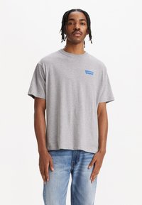Camiseta gris de manga corta hecha de algodón. Presenta un logo azul de Levi's en la zona del pecho izquierdo, con un corte holgado y sin patrones adicionales.