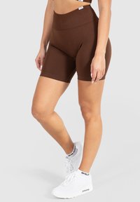 Bruine high-waisted fietsshorts met een gestructureerde afwerking, met een geribbeld elastiek. Gemaakt met witte sneakers voor contrast.