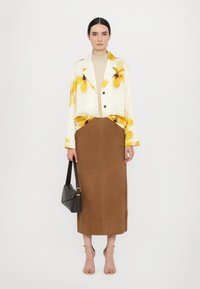 Long-sleeve blazer with yellow floral design, paired with a brown suede midi skirt. Black handbag and beige heeled sandals complete the look.