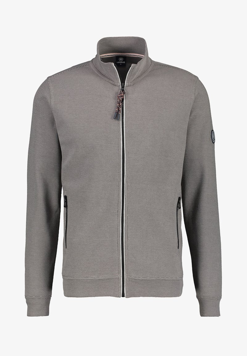 Veste grise à fermeture éclair avec un col montant, tissu tricoté texturé, deux poches latérales zippées, et un patch logo sur la manche gauche.