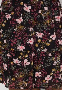 Robe noire à fleurs avec des motifs roses, jaunes et verts. Conçue avec une jupe évasée plissée à étages, fabriquée en tissu léger.