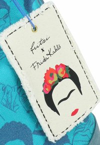 Etichetta tessile blu con un design grafico del volto di una donna con fiori nei capelli. Bordo in tessuto bianco con cucitura nera e un anello blu.