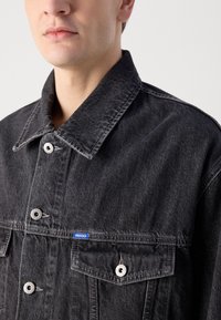 Sort denimjakke med spids krave, sølvtrykknapper og en blå label. Har to brystlommer og en afslappet pasform.
