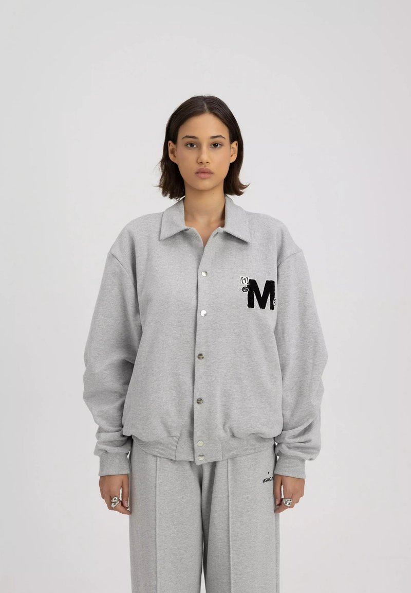 Grijze button-up sweatshirt met kraag, oversized pasvorm en zwart geborduurd "M" logo op de linkerkant van de borst. Zachte textuur en geribbelde manchetten.