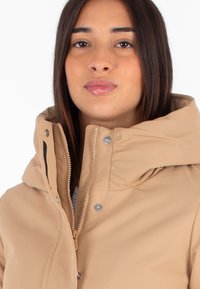 Beige puffer jacket met een hoge kraag, voorrits en drukknoopjes. Materiaal heeft een gladde textuur en een minimalistisch ontwerp.