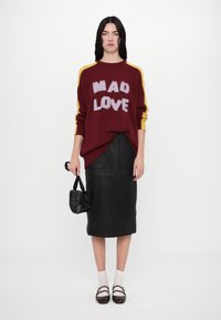 Maroon sweater with "MAD LOVE" in textured lettering, yellow sleeve stripes; black leather midi skirt; black handbag and brown shoes with straps.
