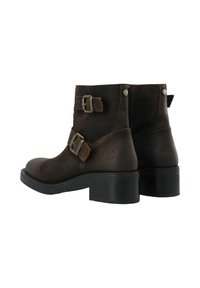 Botas de cuero marrón hasta el tobillo con dos correas ajustables y herrajes plateados, que presentan un tacón bajo y una suela texturizada.