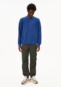 Blauwe crewneck sweatshirt met ribgebreide manchetten, gecombineerd met olijfgroene cargobroeken met zijzakken en grijze sneakers.