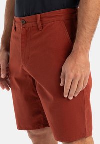 Rust-colored shorts, made of cotton, with a flat front, belt loops, and a single button closure. Smooth texture and straight cut design.