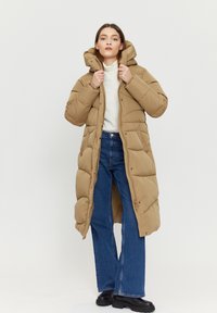 Long brown puffer coat with a hood, featuring a quilted texture, snap buttons, and a straight silhouette, paired with blue flared jeans.