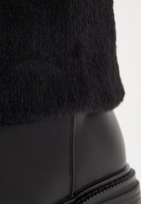 Botine negre până la gleznă, cu o bază din piele netedă și o guler din blană texturată, puțin fuzzy, accentuat de detalii cusute discrete.