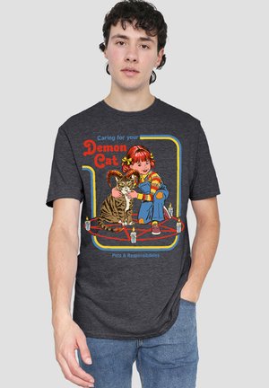 Young man wearing dark gray tee with colorful cartoon girl hugging a horned cat inside a pentagram with candles.