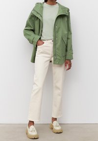 Zielona lekka kurtka z kapturem, zestawiona z jasnozieloną koszulką, jasnoszarymi prostymi dżinsami i kremowymi, grubymi loafersami.