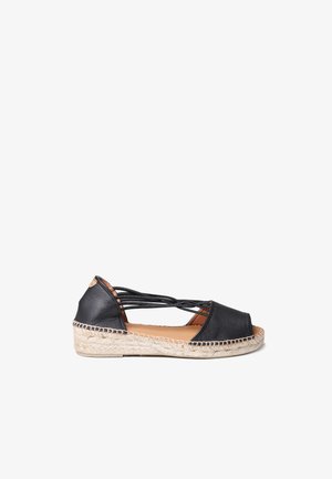 Fekete bőr espadrille nyitott orral, keresztpántos kialakítással és juta borítású wedge sarokkal. Simaság és minimalista dizájn jellemzi.
