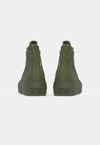 Zelene visoke tenisice od glatkog platna, gumeni potplati i Converse All Star oznaka na stražnjoj i bočnoj strani. Primjećena značajka otpornosti na vodu.