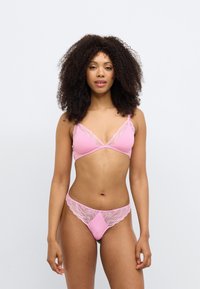 Růžový souprava spodního prádla s krajkou, která obsahuje braletku s trojúhelníkovými košíčky a k ní ladící tanga; hladká textura, jemné krajkové detaily.