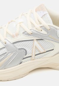 Baskets légères avec une tige en mesh blanc et gris pâle, accents beiges, couture détaillée et lacets ronds.
