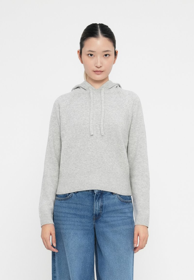 Felpa grigia chiara realizzata in morbido materiale a maglia, con cordino, orlo a coste e vestibilità rilassata, abbinata a jeans larghi blu.