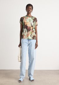 Blomstertrykt kortermet skjorte i mørkebrun, med grønne, oransje og gule blader. Kombinert med lyseblå jeans og åpne blå hæler.