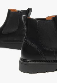 Bottines en cuir noir avec des panneaux latéraux élastiques, des détails en brogue et une finition lisse. Semelle en caoutchouc épaisse pour une meilleure traction.
