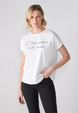 White cotton t-shirt with rolled sleeves featuring black cursive text "To the moon and back" across the front. Paired with black jeans.