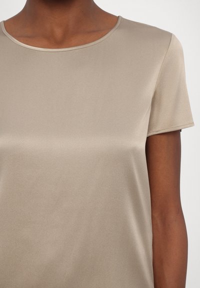 Top bege de manga curta feito de um tecido suave e liso, com decote redondo e um brilho subtil. Detalhes de costura ao redor das mangas.