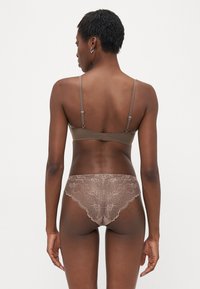 Woman wearing taupe bra and matching lace underwear, shown from the back against a plain white background.