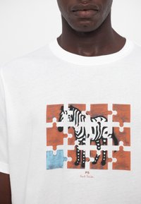 Gros plan d'une chemise blanche avec un graphisme puzzle montrant un zèbre, une pièce bleue du puzzle manquante dans le coin inférieur gauche.