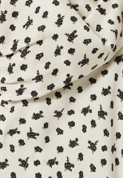 Tejido crema con pequeño patrón floral negro. Presenta una textura suave y un brillo sutil. El diseño incluye grupos de flores con tallos.