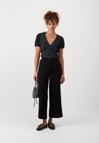 Top nero a maniche puff con scollatura a V, abbinato a pantaloni neri a gamba larga. Gli accessori includono una mini borsa a fantasia e sandali neri flat.