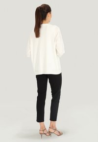 Biała bluzka z długim rękawem o luźnym kroju, zestawiona z czarnymi spodniami o slim fit oraz cielistymi sandałami na obcasie z teksturowanym wzorem.