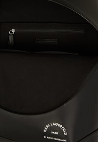 Rucsac negru cu un exterior neted, având un compartiment cu fermoar, căptușeală din material textil și un etichetă cu "KARL LAGERFELD PARIS" embosată.