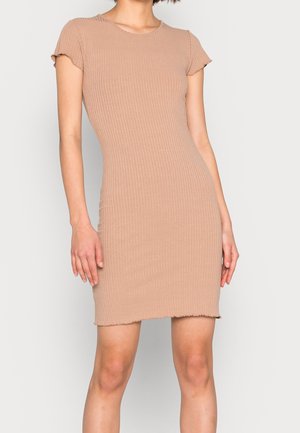 Beige geribbelde bodycon-jurk met korte mouwen en gegolfde zoom, gedragen door een staand persoon tegen een effen lichte achtergrond.