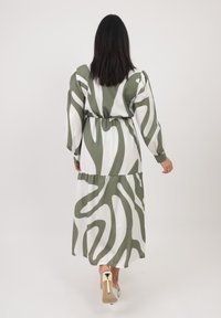 Abito lungo bianco con motivo astratto verde, dotato di maniche a sbuffo e vita elastica. Tessuto morbido con un design fluido.